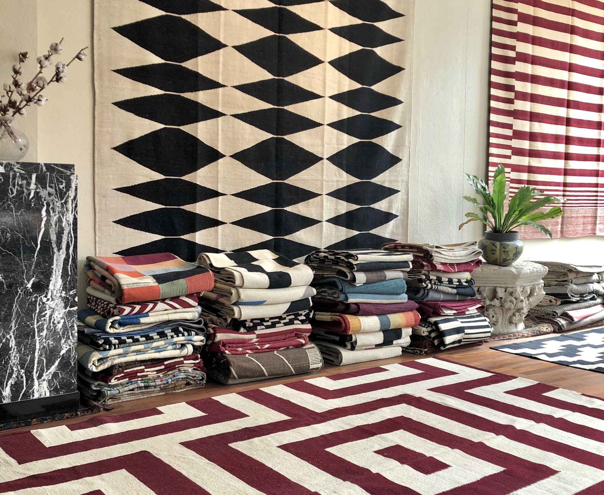 Gevouwen textielstapels op houten vloer, met geometrische wandtapijten en rode gestreepte gordijnen.