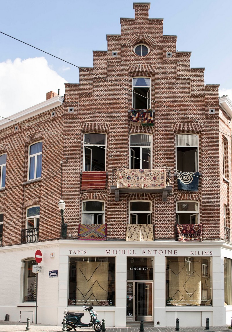 Bakstenen gevel met ronde boogramen, balkons met tapijten en winkelpui onder blauwe lucht.