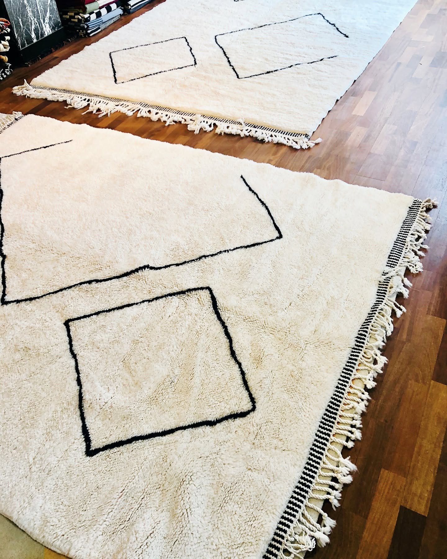 Witte vloerkleden met zwarte ruitlijnen en franjes op houten vloer, in een lichte woonkamerhoek.